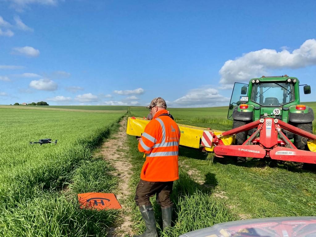 Pilot der Kitzrettung steuert die Drohne neben einem startbereiten Mähwerk und Traktor
